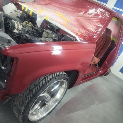 A red car with the hood open is sitting in a garage.