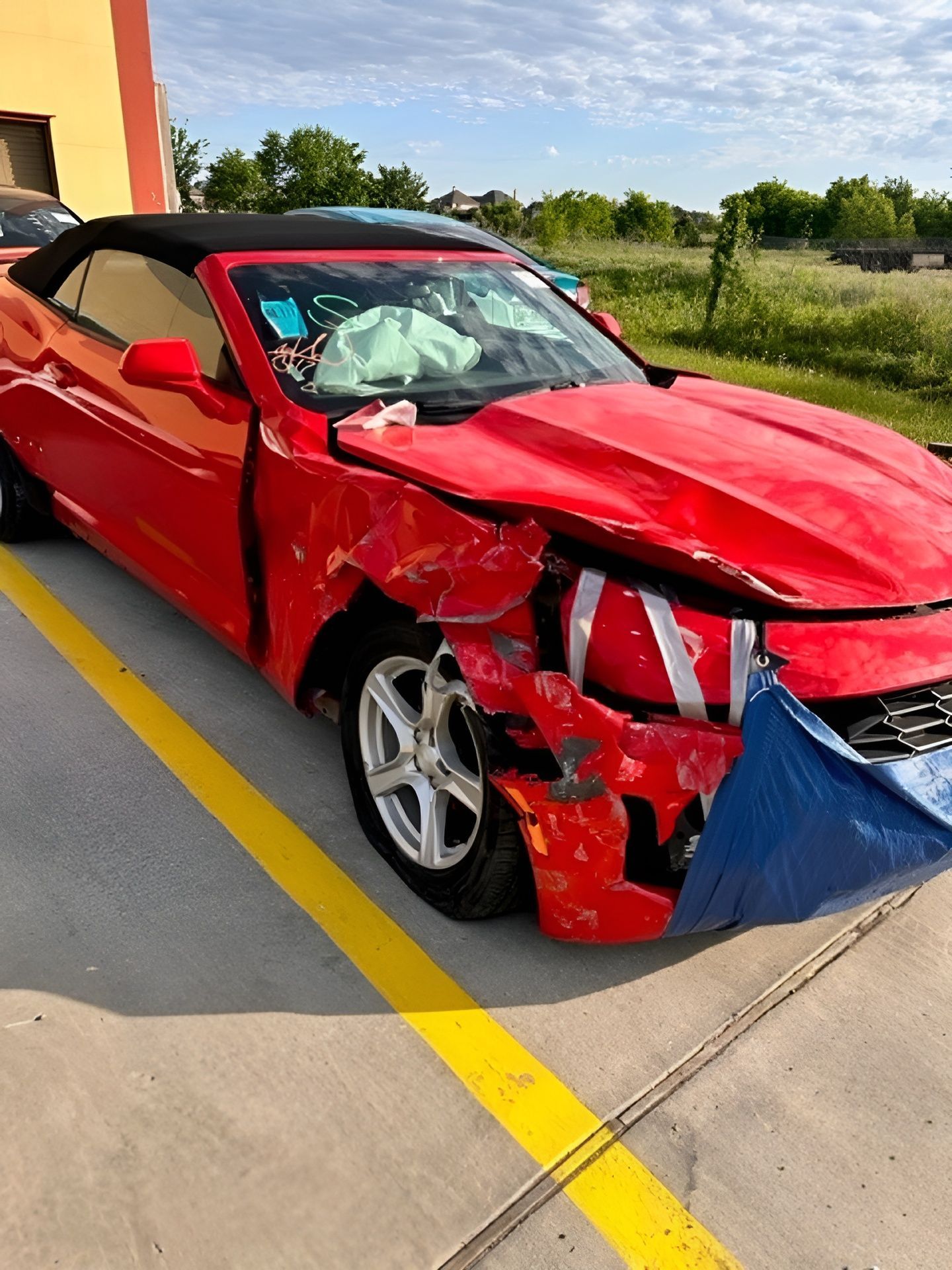 A red car with a damaged front end is parked in a parking lot.