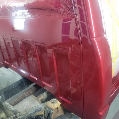 A red truck is parked in a garage and is being painted.