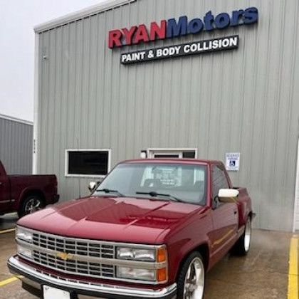 A red truck is parked in front of ryan motors paint and body collision.