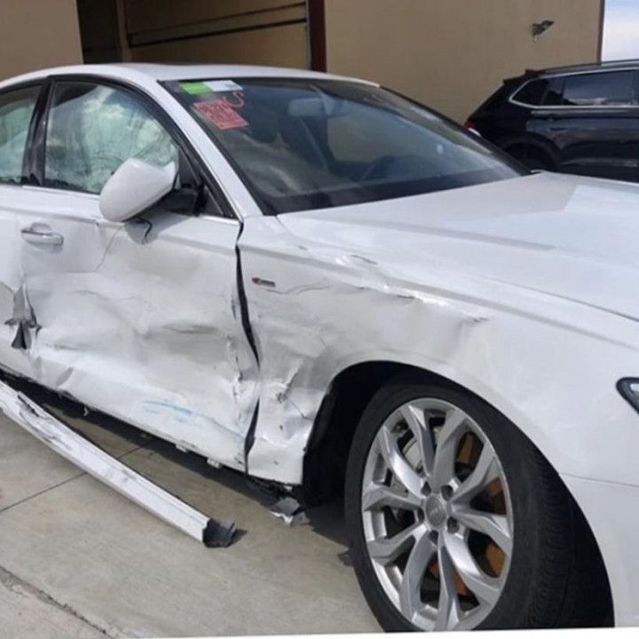 A white car with a damaged side is parked in front of a building.