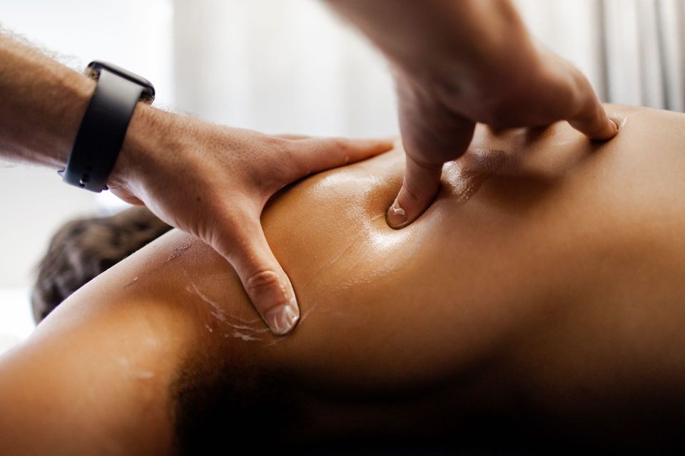 Person receiving back massage, hands applying pressure to shoulder.
