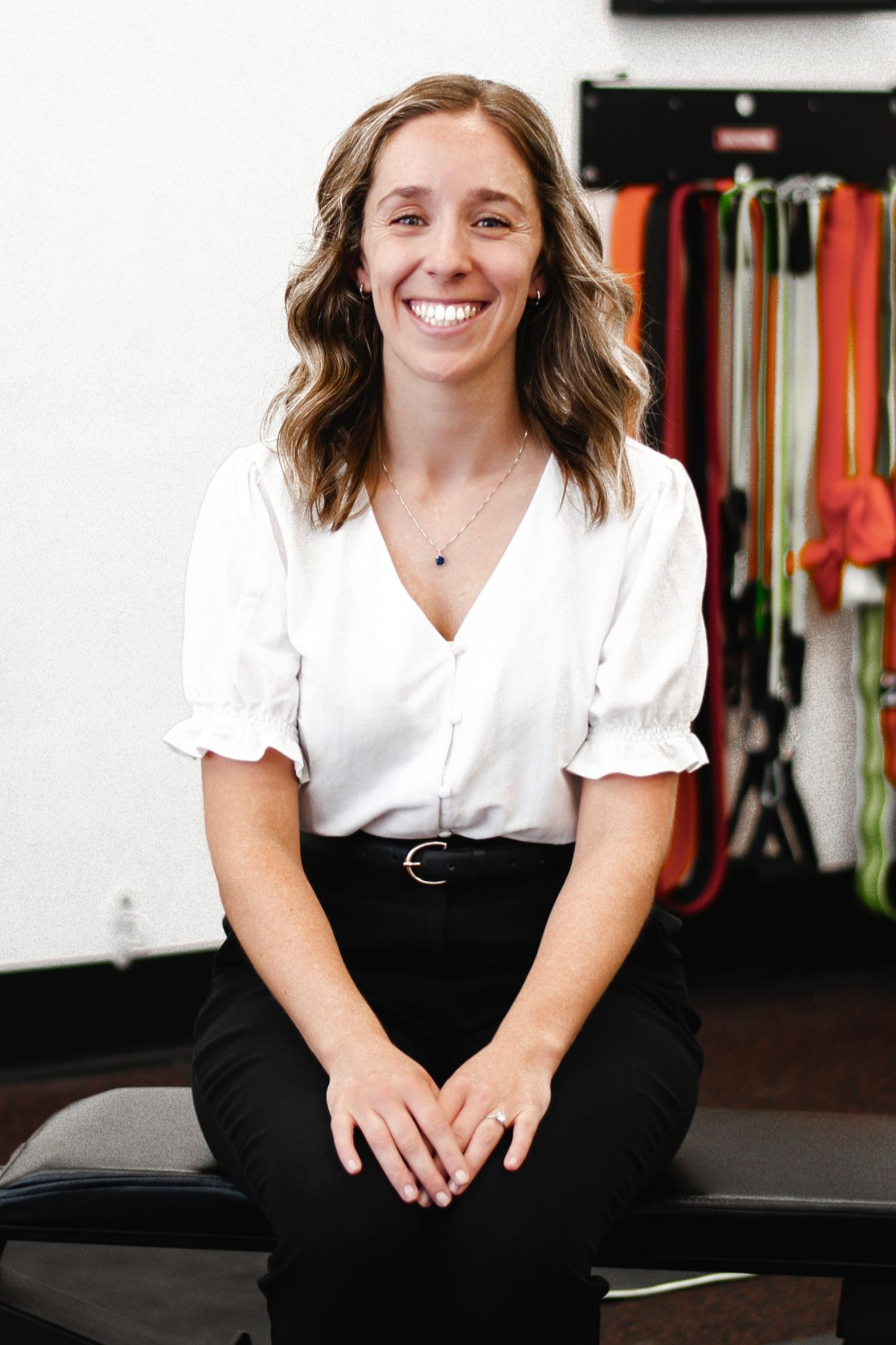 Man in white shirt smiling, seated on weight bench near gym equipment.
