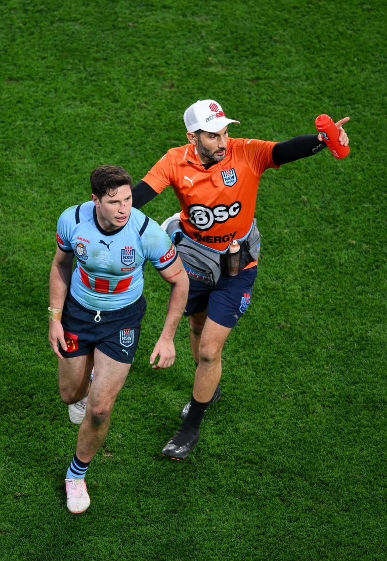 Man in blue jersey runs on field with official in orange, pointing.