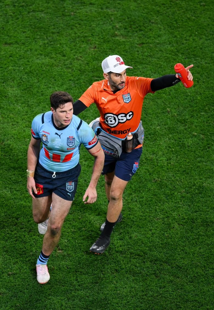 Man in blue jersey runs on field with official in orange, pointing.