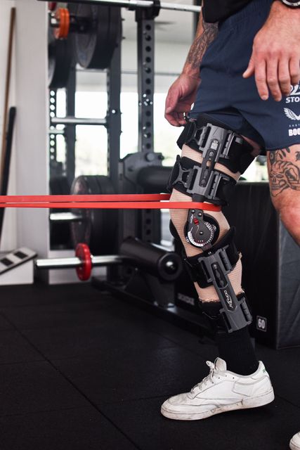 Person with leg brace doing exercise with resistance band in gym.