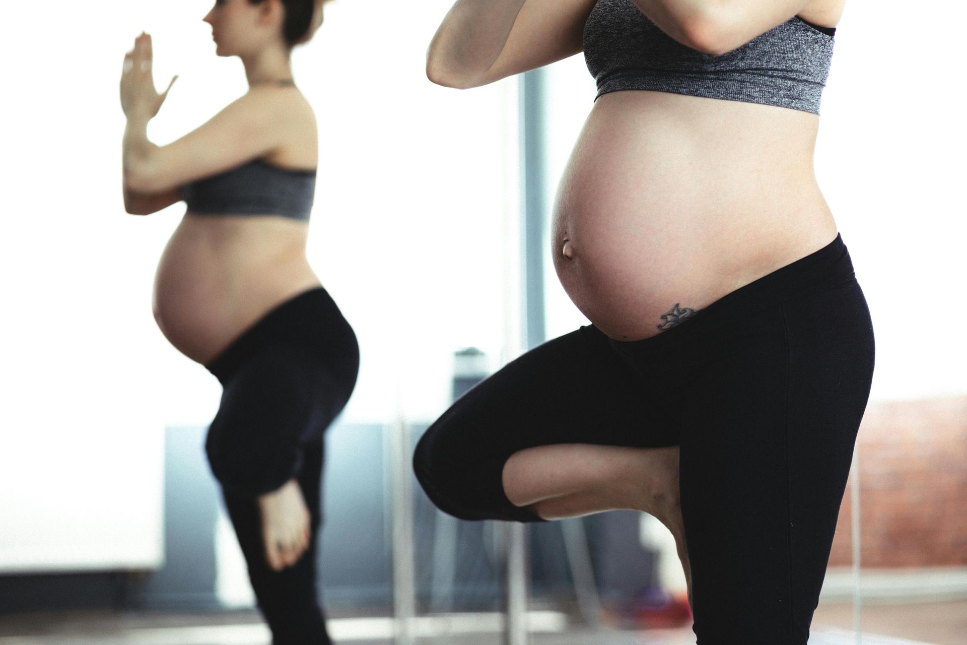 Pregnant woman practicing yoga balance pose in a bright studio, reflected in a mirror