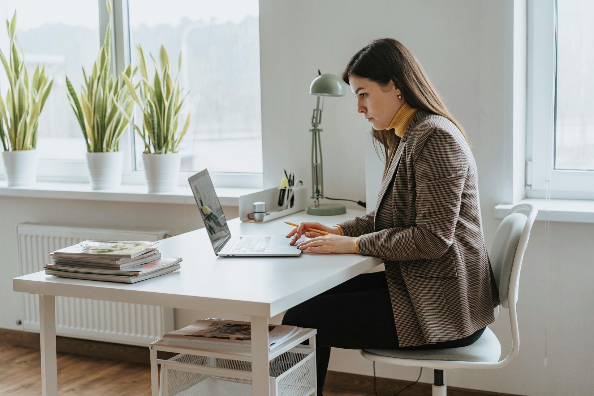 Woman working on a laptop at a bright desk in a minimalist office by a window