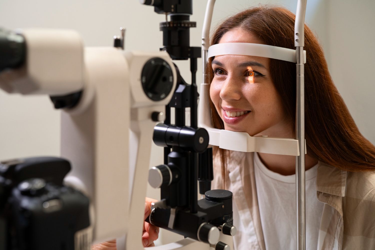 Woman at an eye exam. Light shines into her eye. She smiles while sitting in front of a medical device.