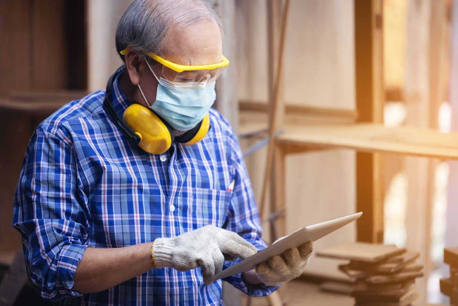 Worker wearing safety gear using a tablet in a woodworking workshop