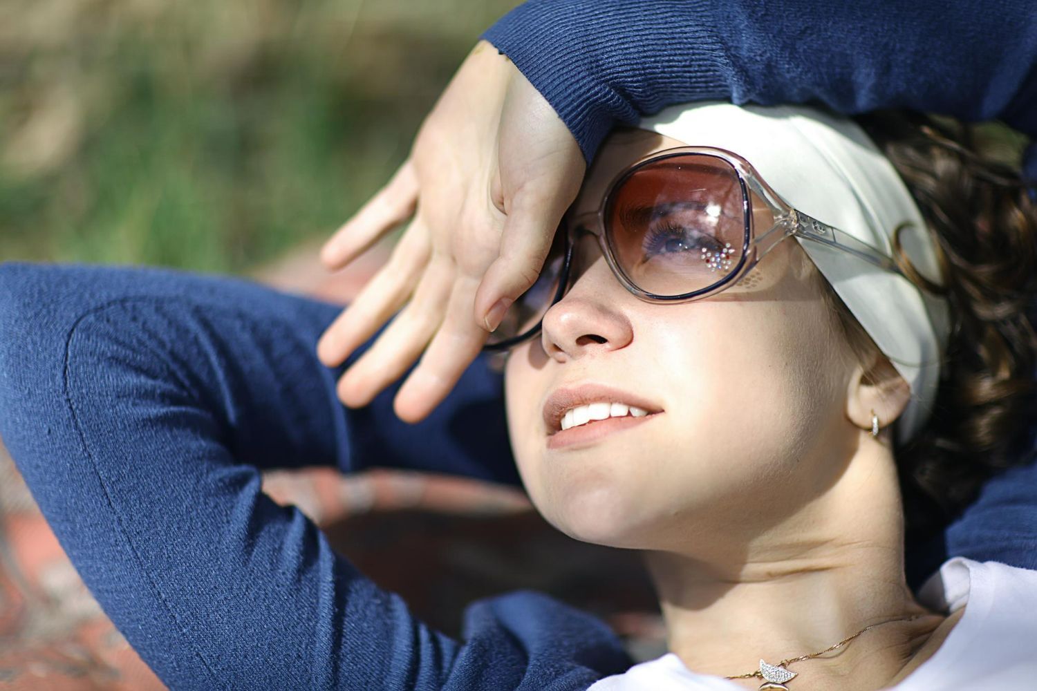 Person reclining outdoors, wearing sunglasses and a headband, shielding their eyes from the sun
