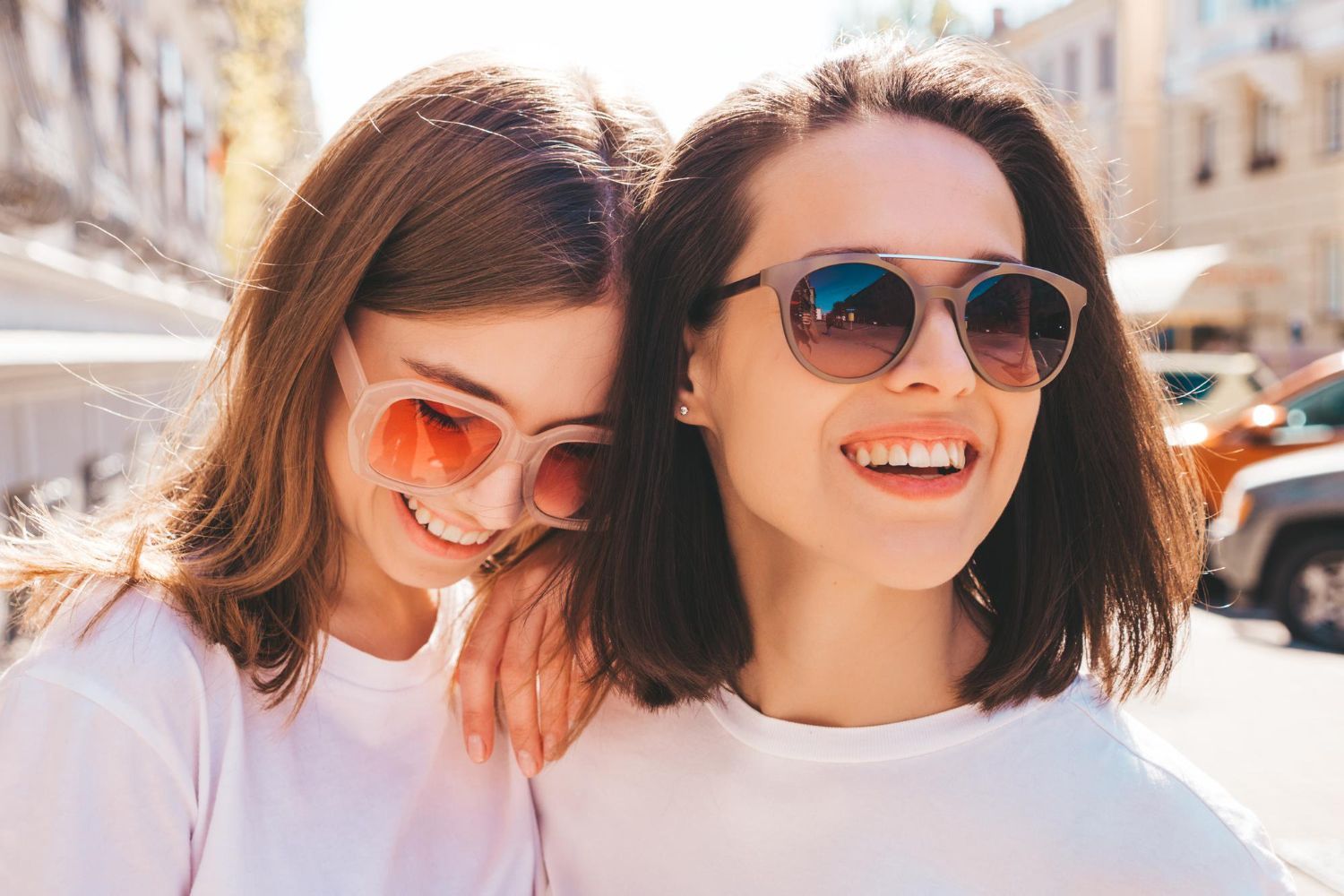Two smiling people in sunglasses embrace outdoors.