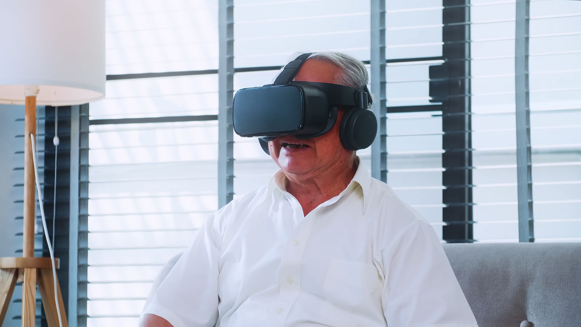 An elderly man is wearing a virtual reality headset while sitting on a couch.