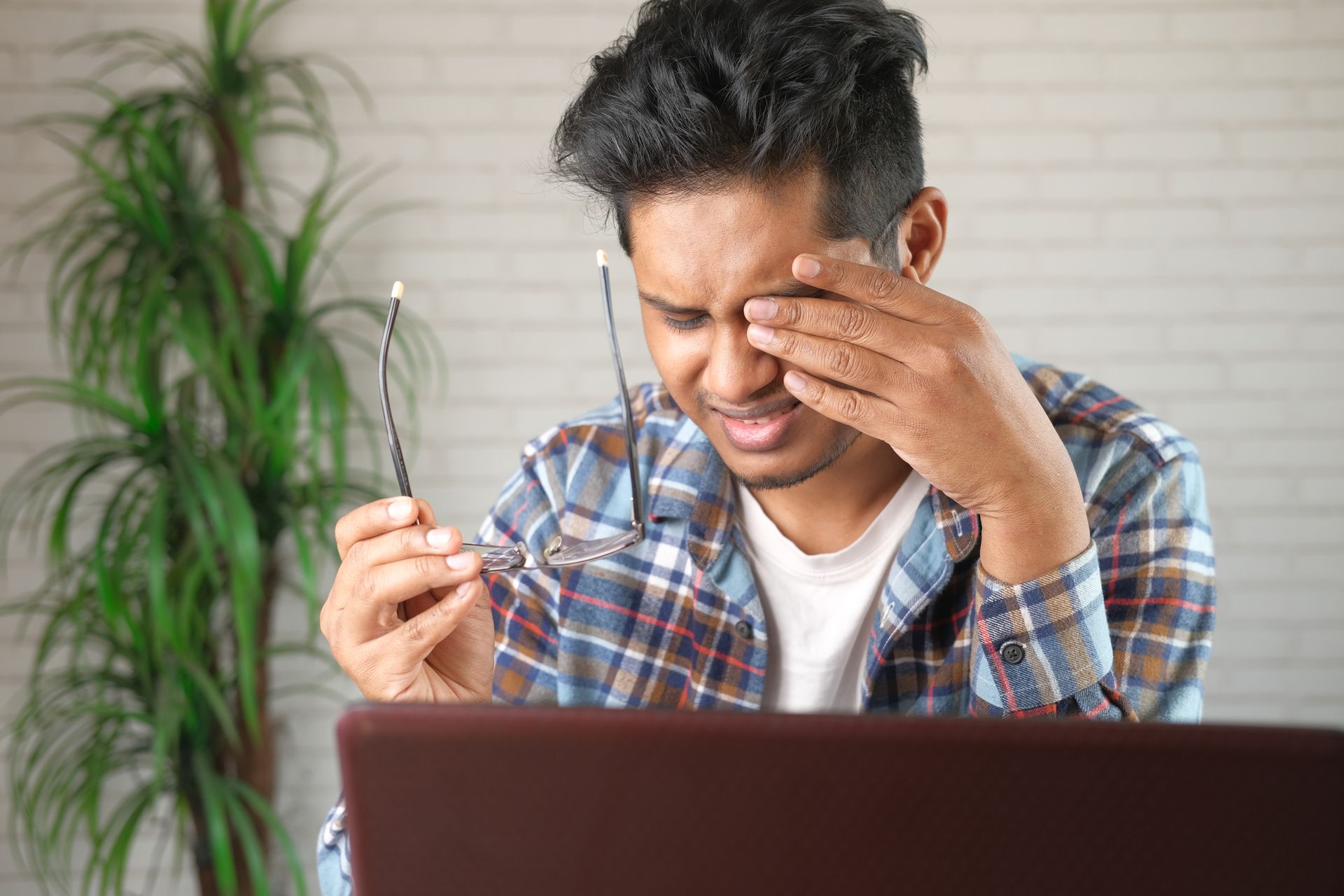 A man is rubbing his eyes while looking at a laptop computer.