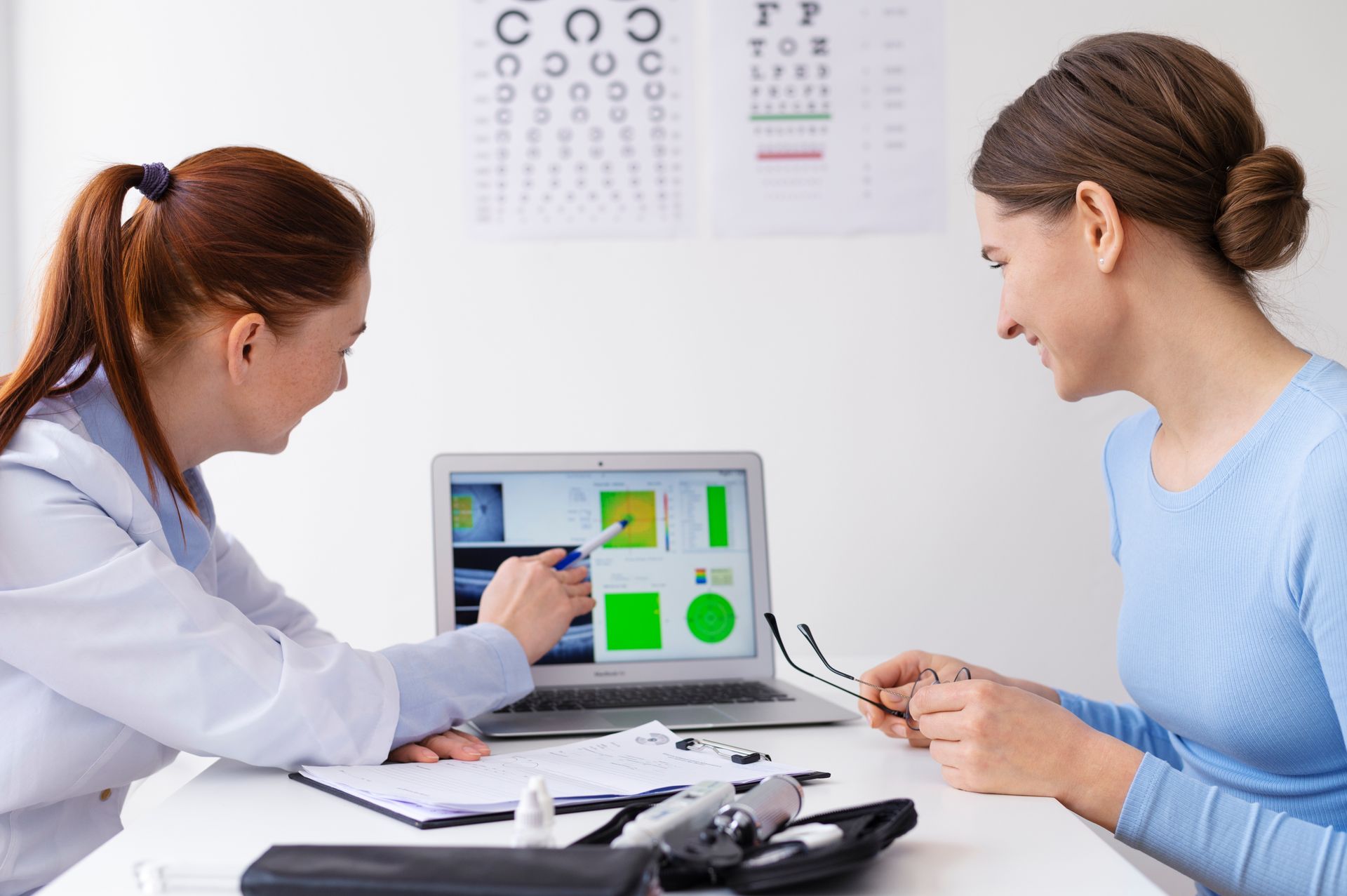 A woman is sitting at a table with a doctor and looking at a laptop.