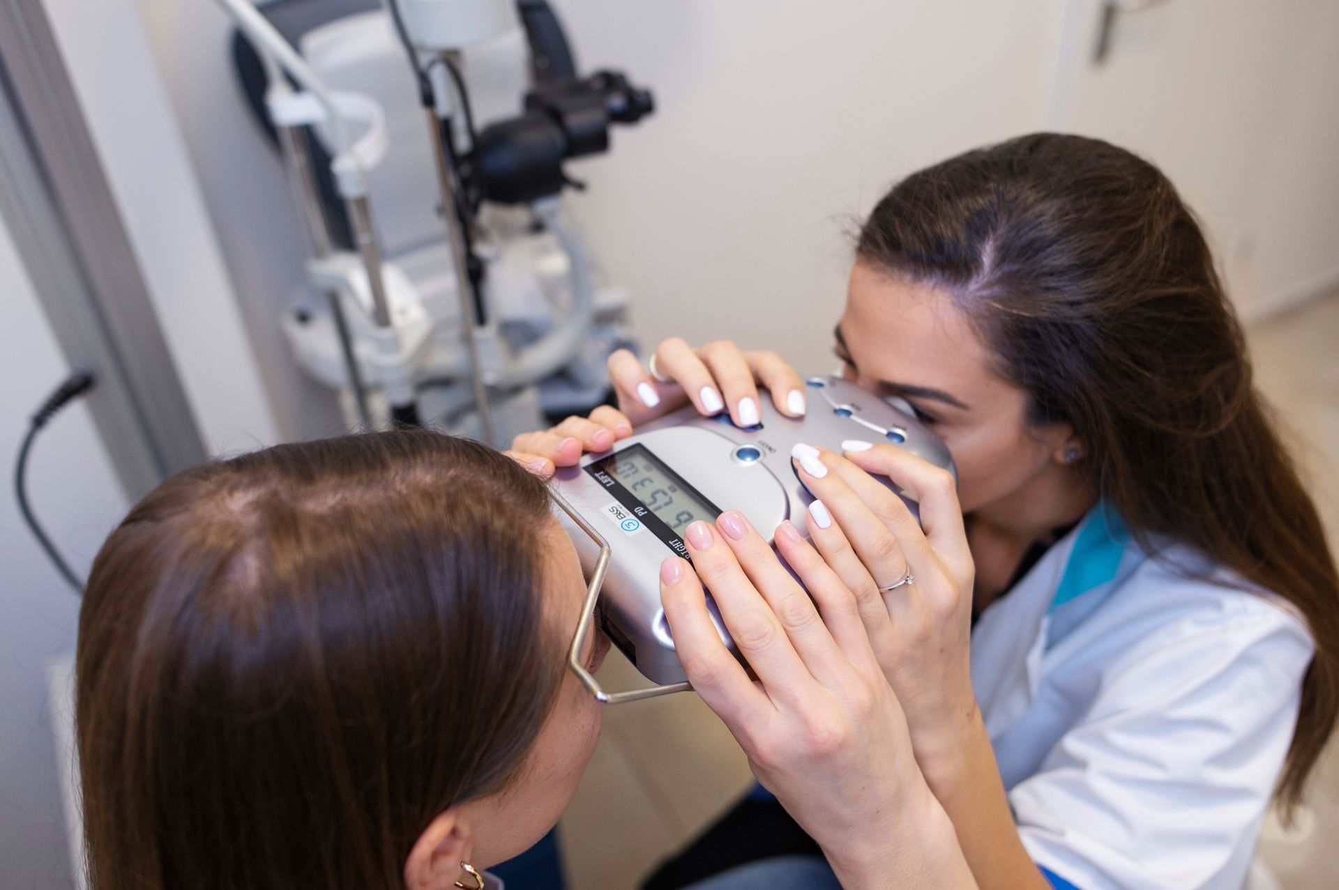 A woman is looking through a microscope at another woman 's hair.