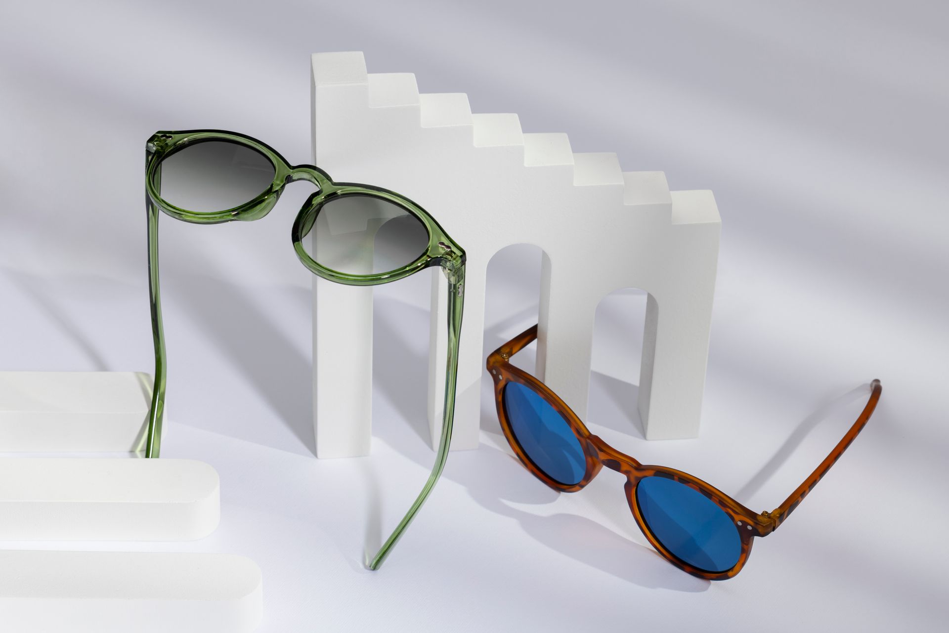 Two pairs of sunglasses are sitting next to each other on a white surface.