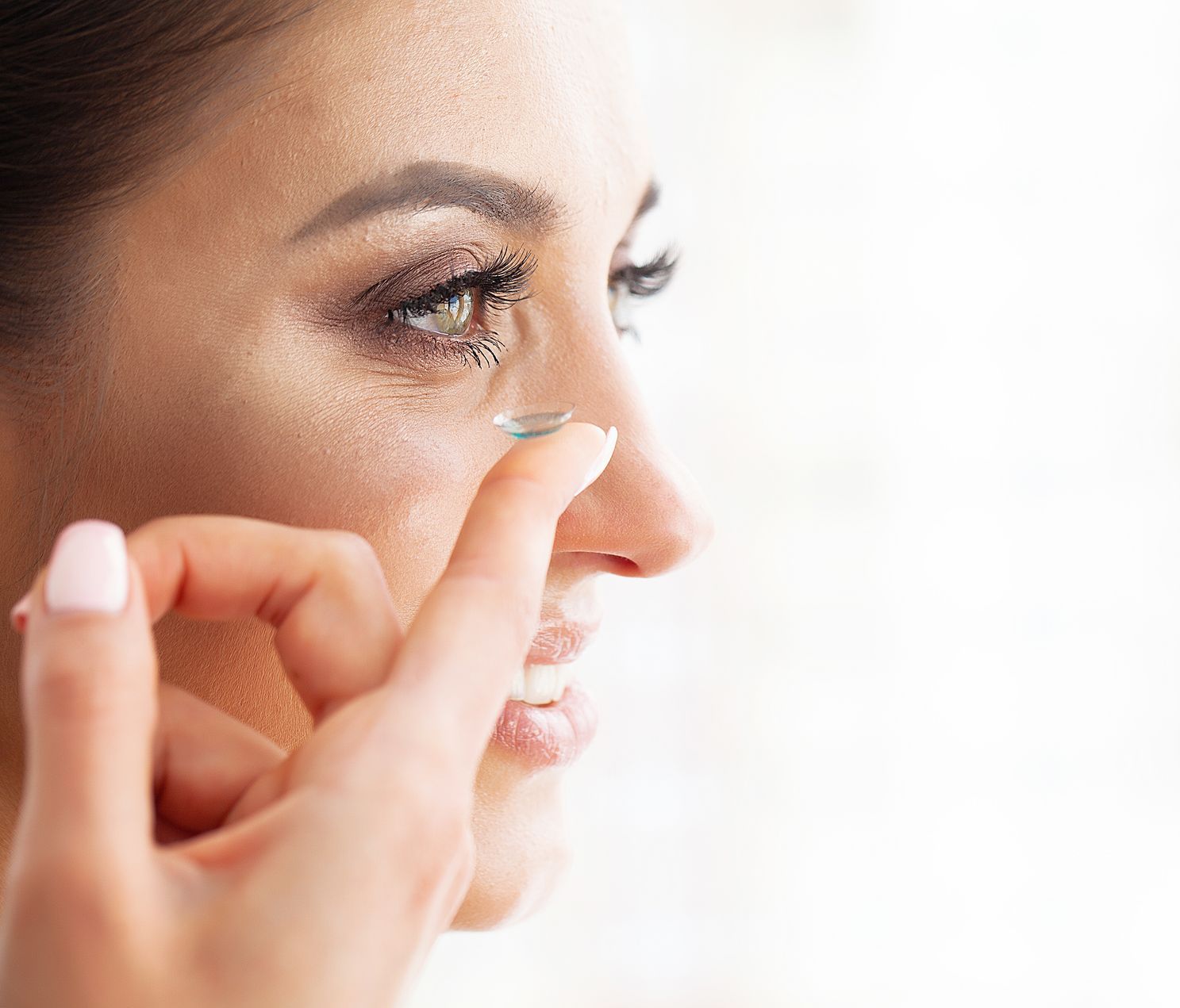 A woman is putting a contact lens in her eye.