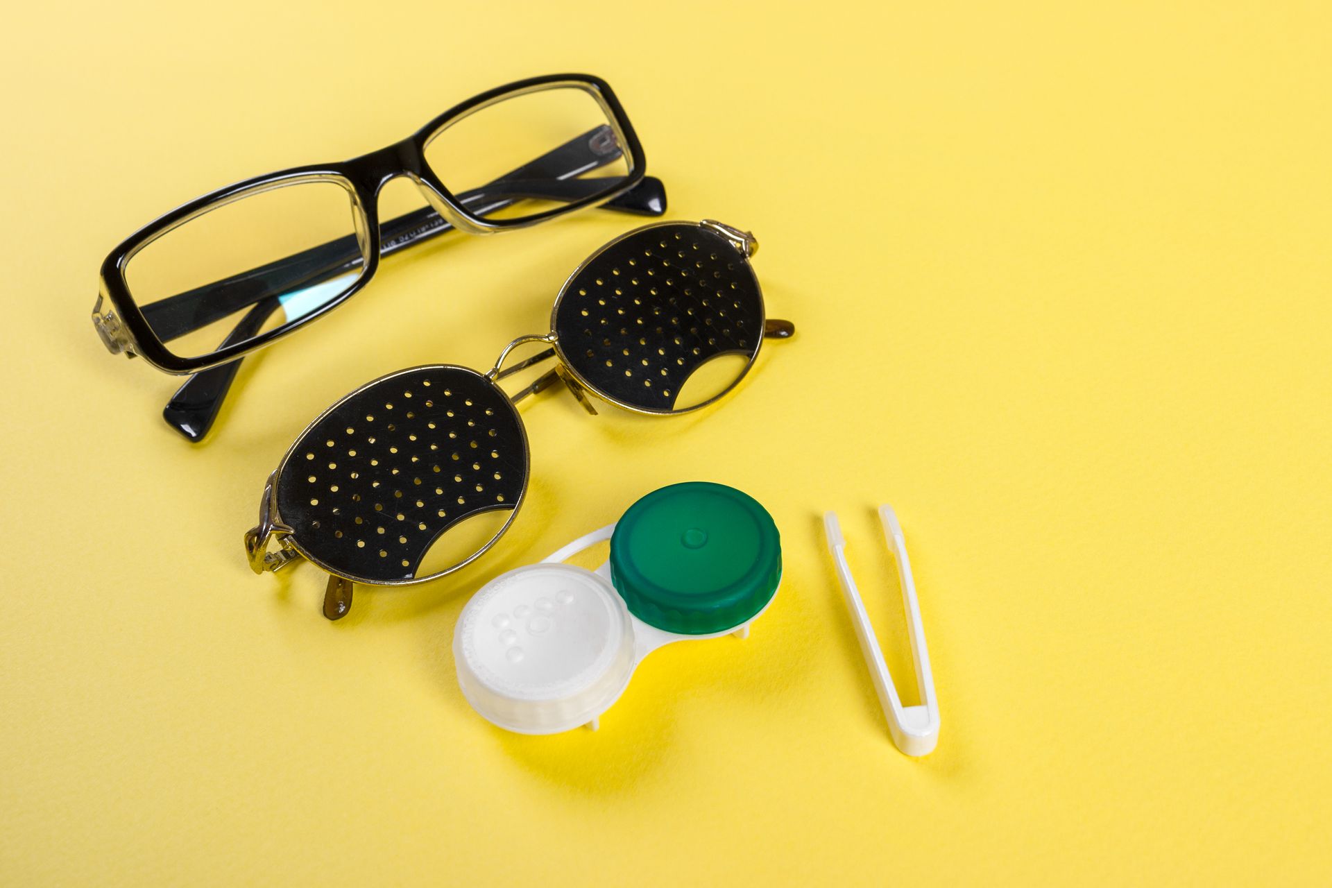 A pair of glasses , a contact lens case , and tweezers on a yellow background.