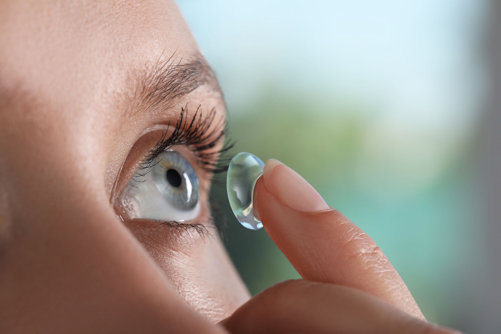 A woman is putting a contact lens in her eye.