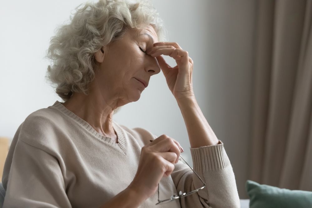 Woman with closed eyes, touching her nose, appears stressed, indoors.