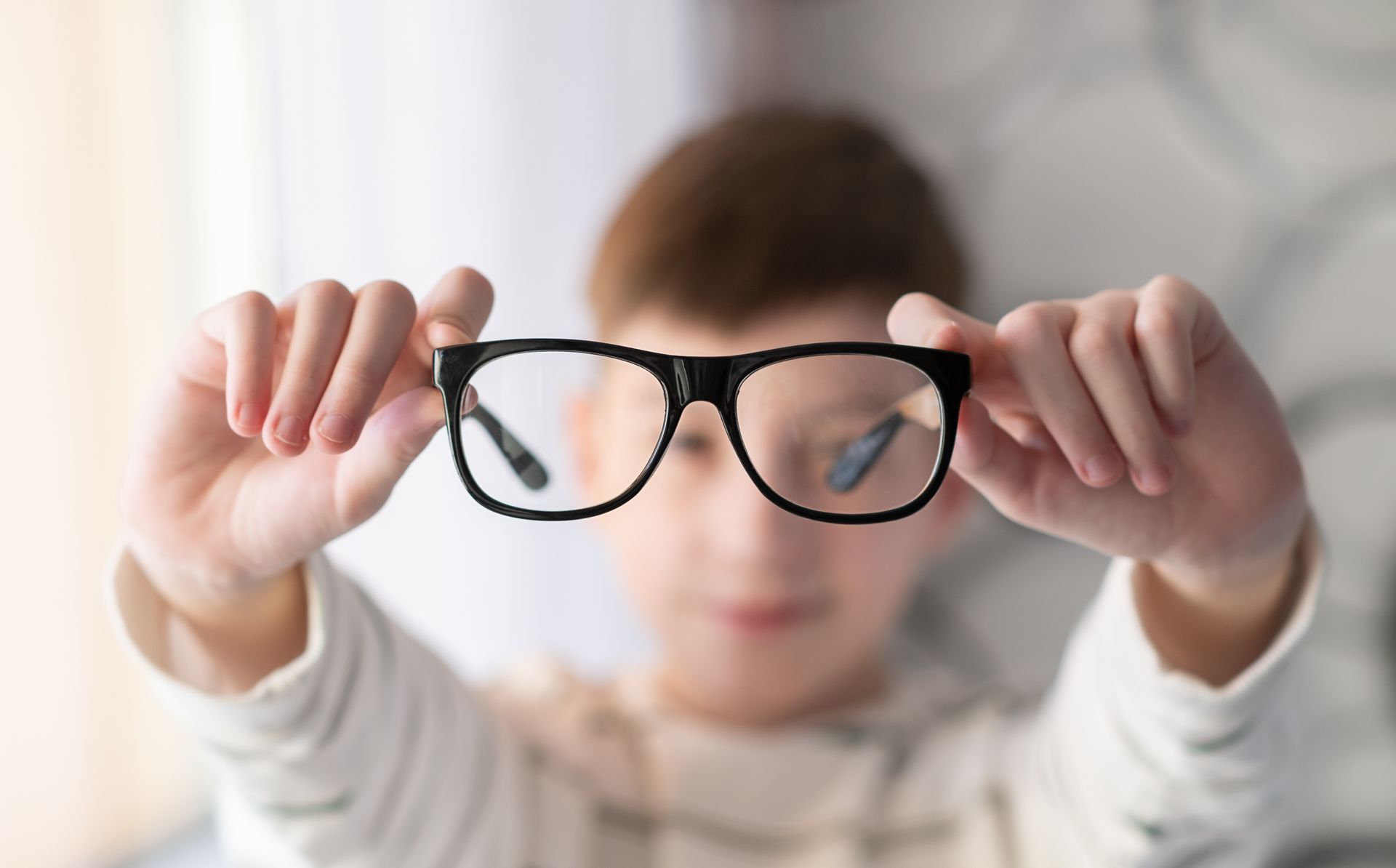 A young boy is holding a pair of glasses in front of his face.