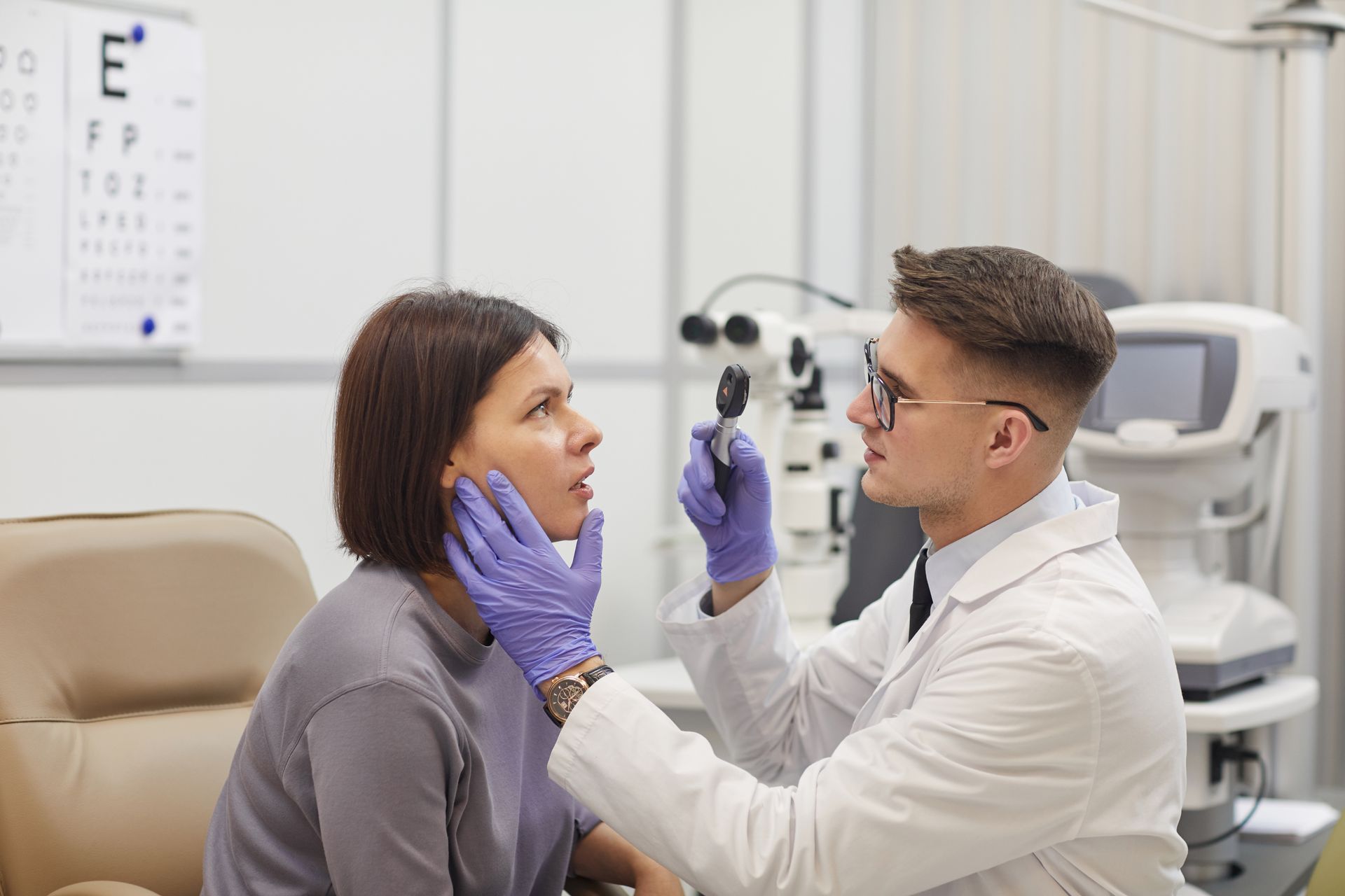 An ophthalmologist is examining a woman 's eye with a microscope.