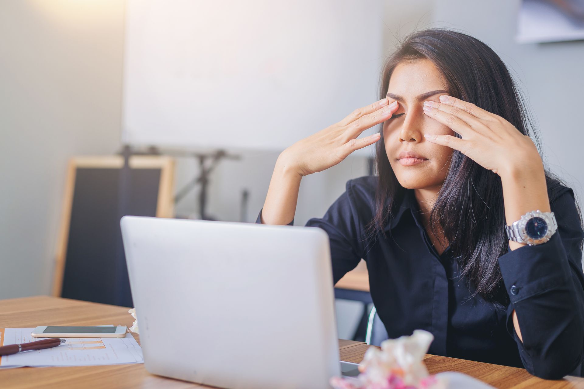 A woman is rubbing her eyes while sitting in front of a laptop computer.