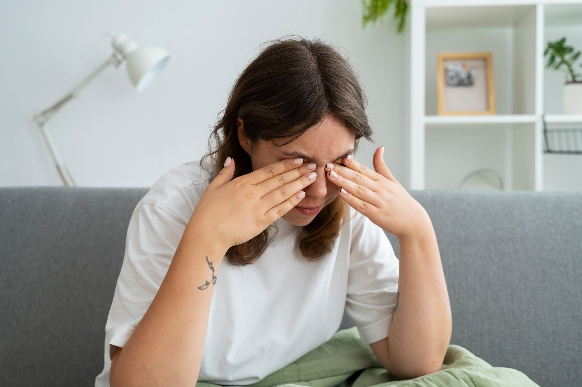 A woman is sitting on a couch rubbing her eyes.