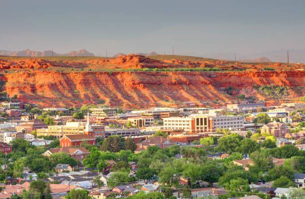 Cityscape with red rock cliffs in the background; buildings and trees in the foreground.