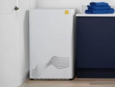 Electric white boiler, installed in the corner of a laundry room with towels next to it.