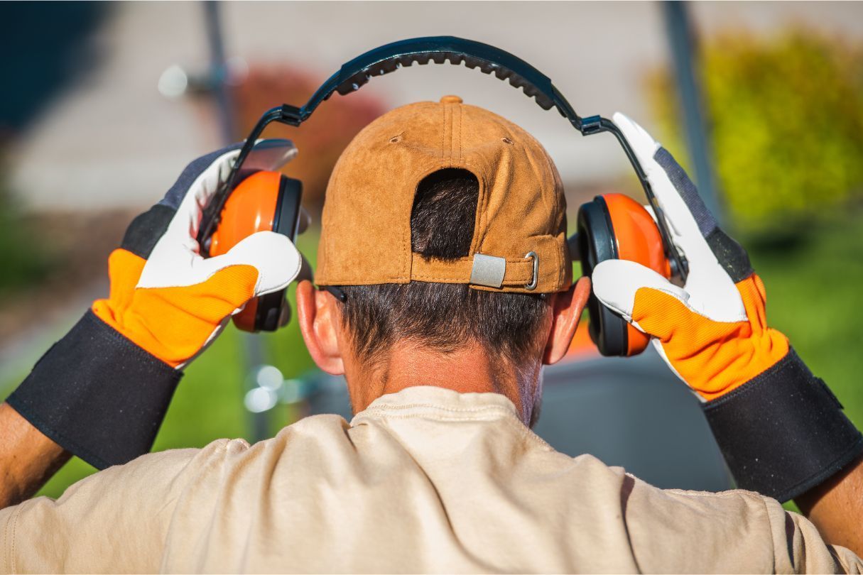 An individual putting on noise reduction headphones in a garden before doing work on the property.