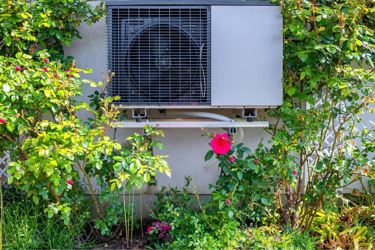 An air source heat pump on a shelf in a garden with green plants around it.