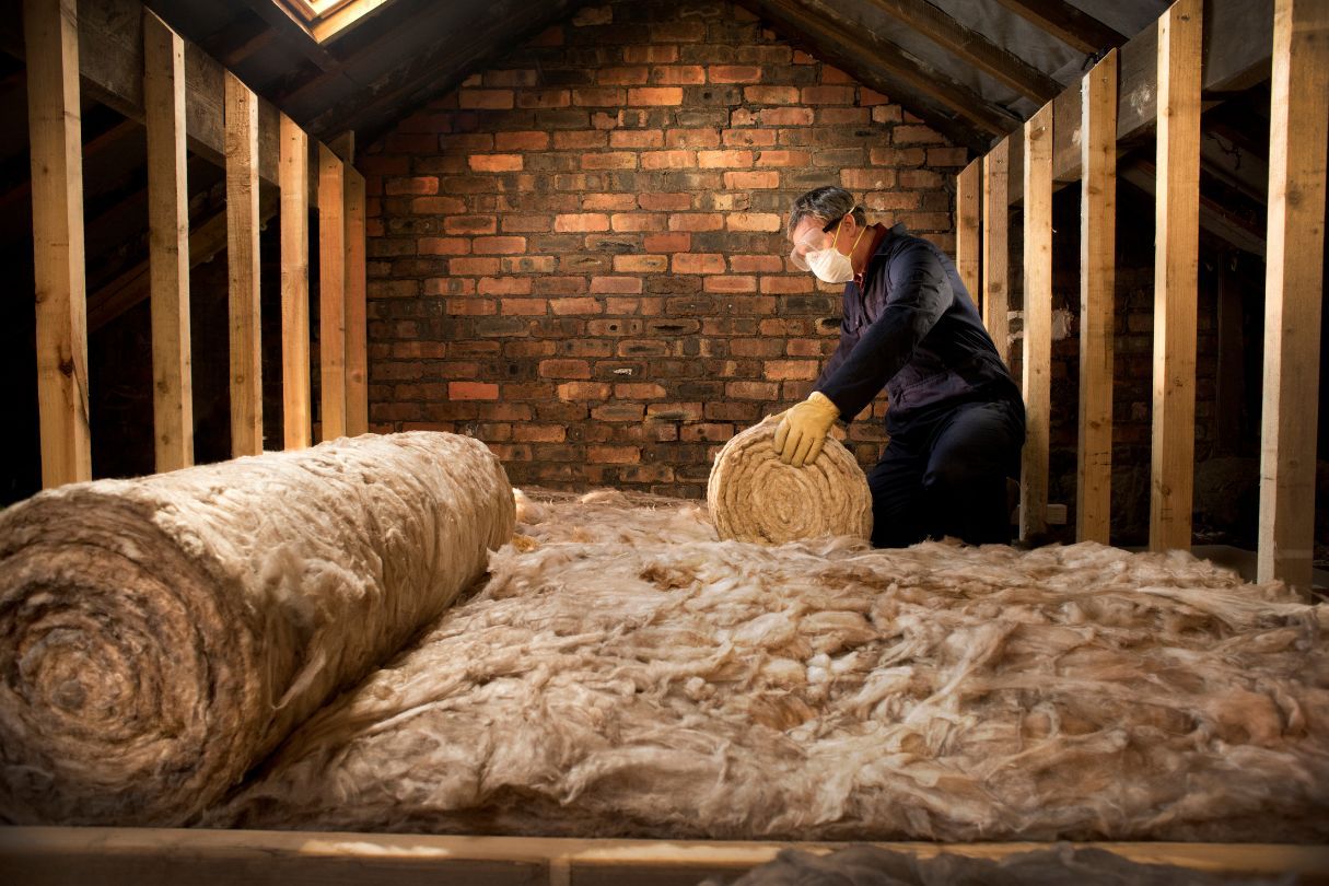 A man with a mask laying insulation in a loft.