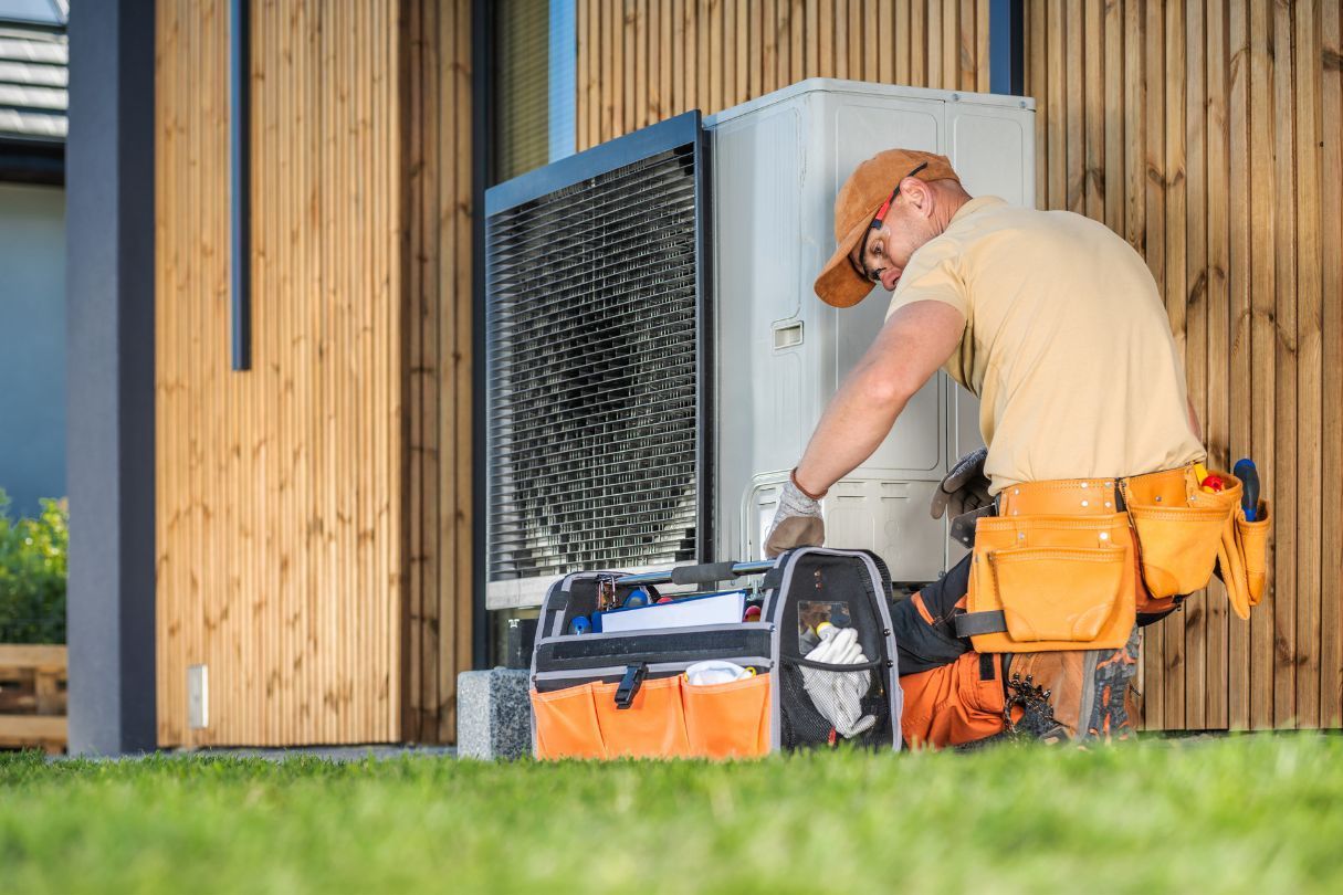 A man is working on a heat pump outside of a house.