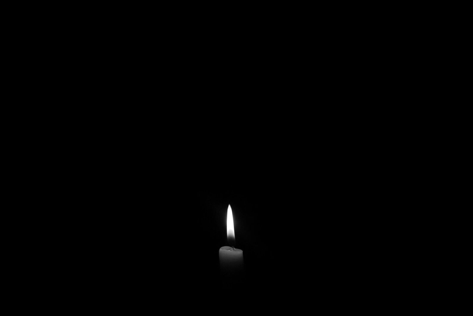 A candle is lit in the dark in a black and white photo.