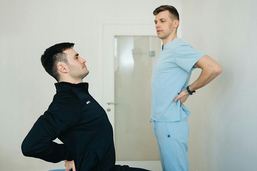 Two men in workout clothes stretching back-to-back in a bright room