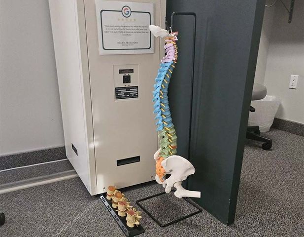 A skeleton dog draped in rainbow lei stands by an office doorway with small pumpkins on the floor.
