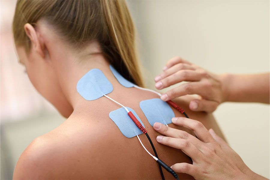 Hands place electrode pads on a person’s upper back and neck for electrotherapy.