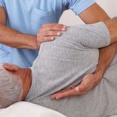 Physical therapist assisting a patient with a side-lying back stretch on a treatment table