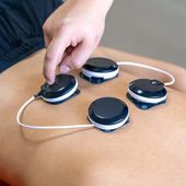Hand placing connected electrode pads on a person’s bare abdomen during a body treatment