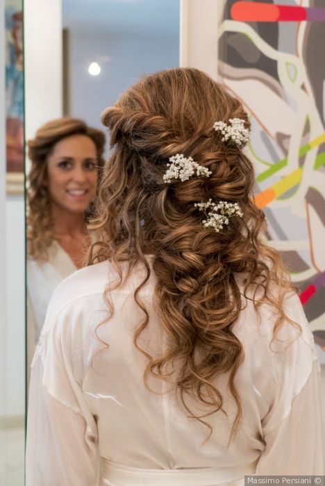 Woman with curly updo, baby's breath, looking at mirror. She's wearing a white robe, smiling.