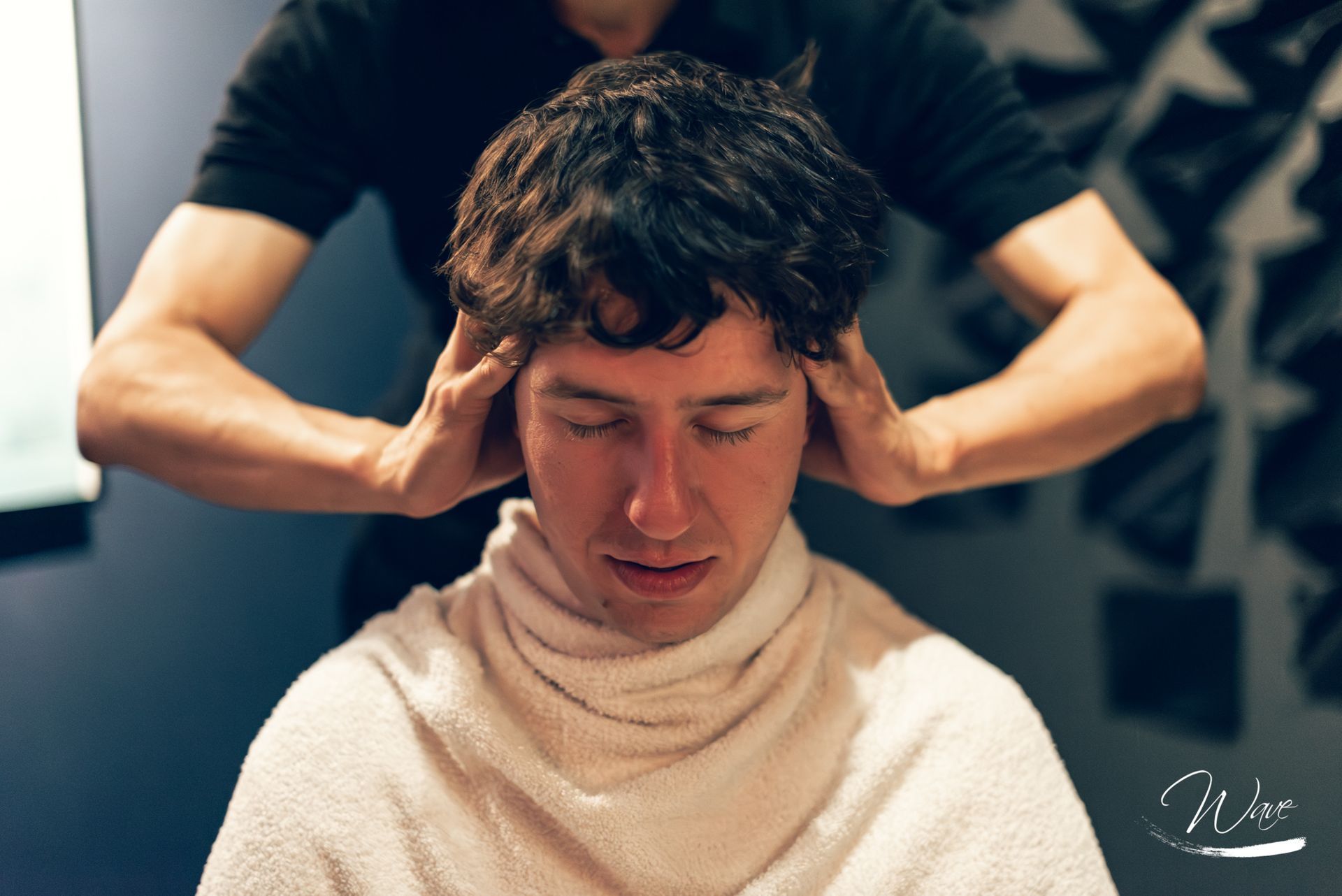 Uomo che riceve un massaggio alla testa in una spa, occhi chiusi, braccia della massaggiatrice dietro di lui.