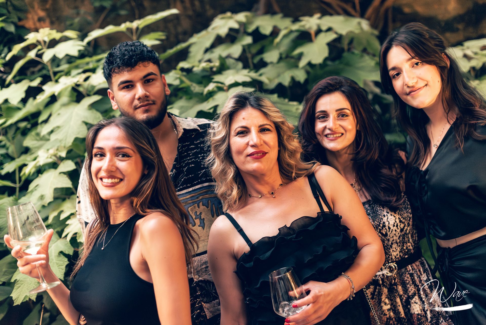 Cinque persone sorridenti davanti a un fogliame verde,