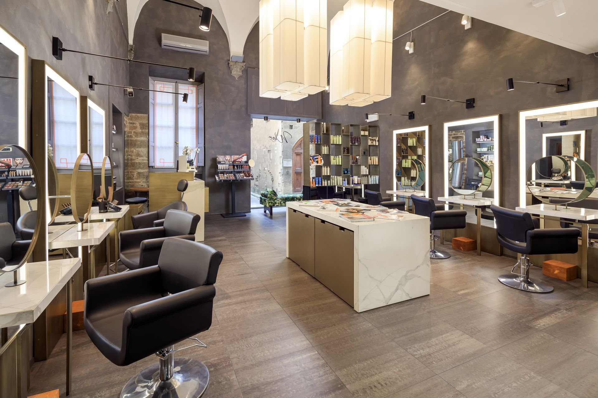 Interno di un salone da parrucchiere con postazioni per lo styling, sedie e tavolo espositivo centrale.