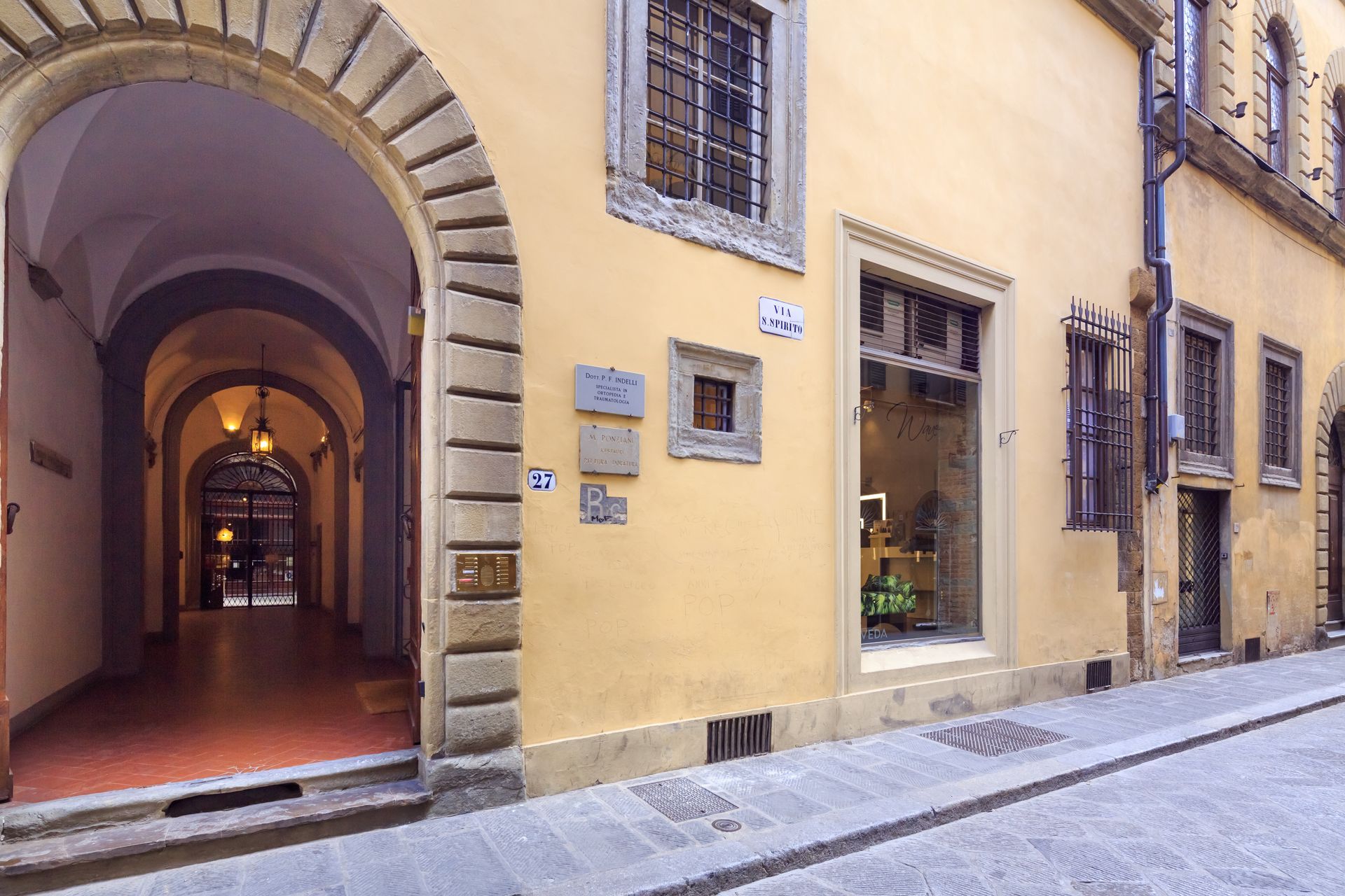 Un ingresso ad arco e una vetrina su una stretta strada acciottolata in una città toscana.