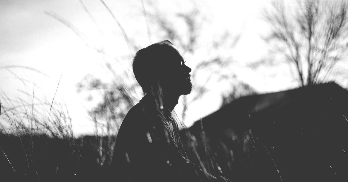 A black and white photo of a man sitting in the grass looking up.