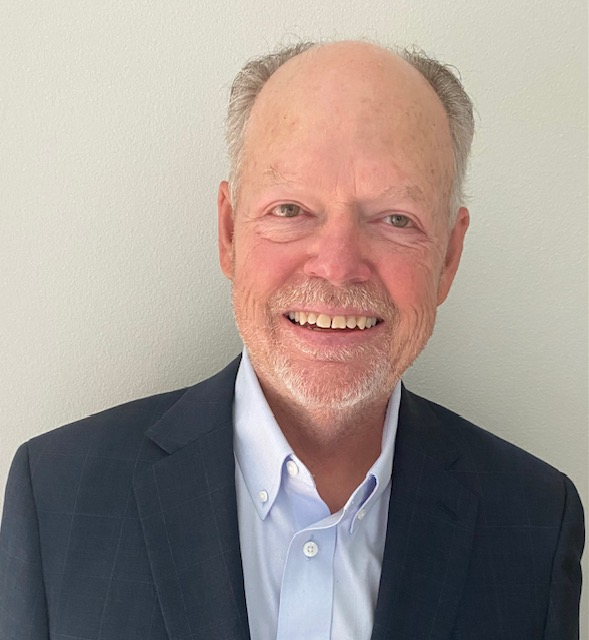 A bald man with a beard is wearing a suit and smiling.