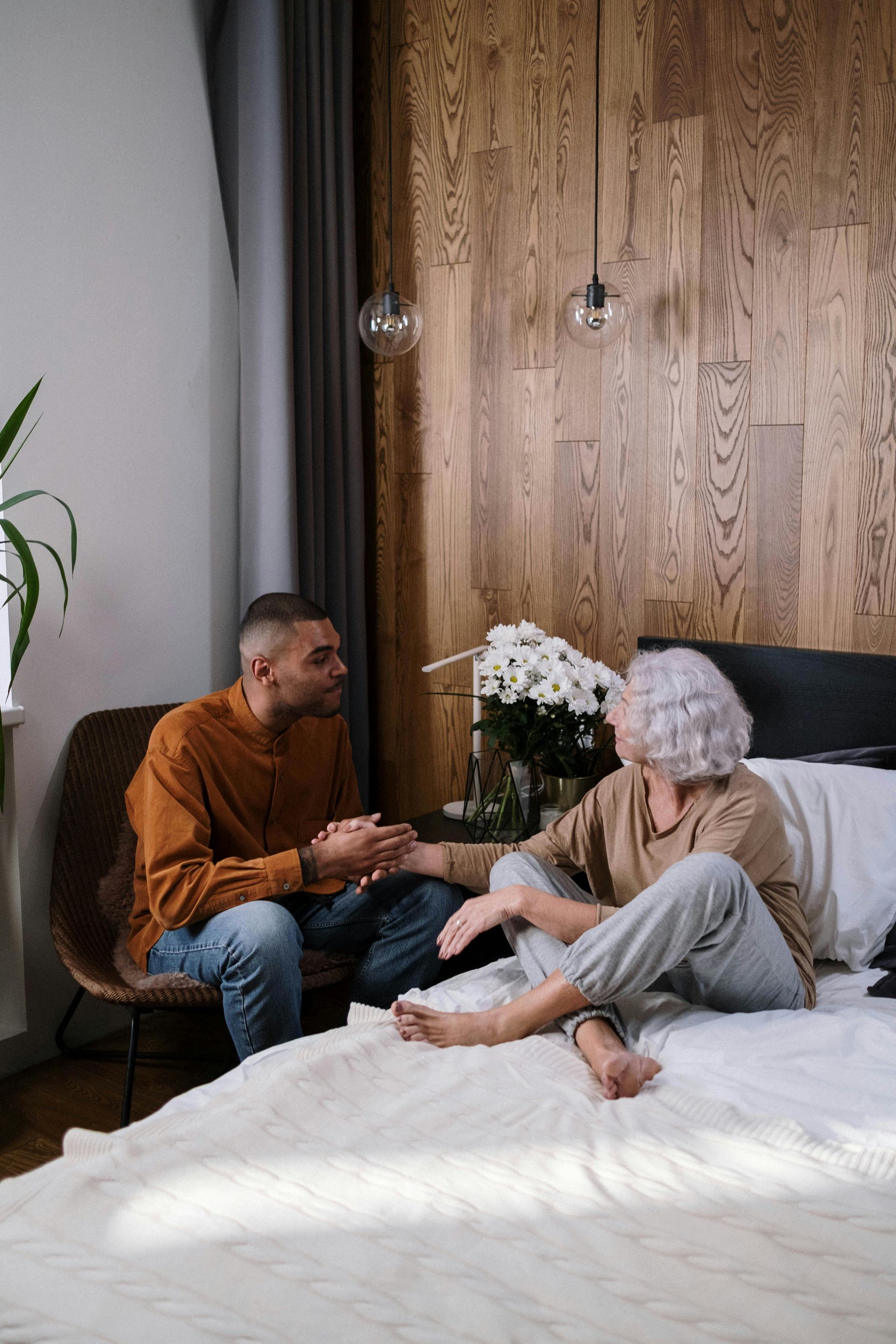 A man and a woman are sitting on a bed talking to each other.