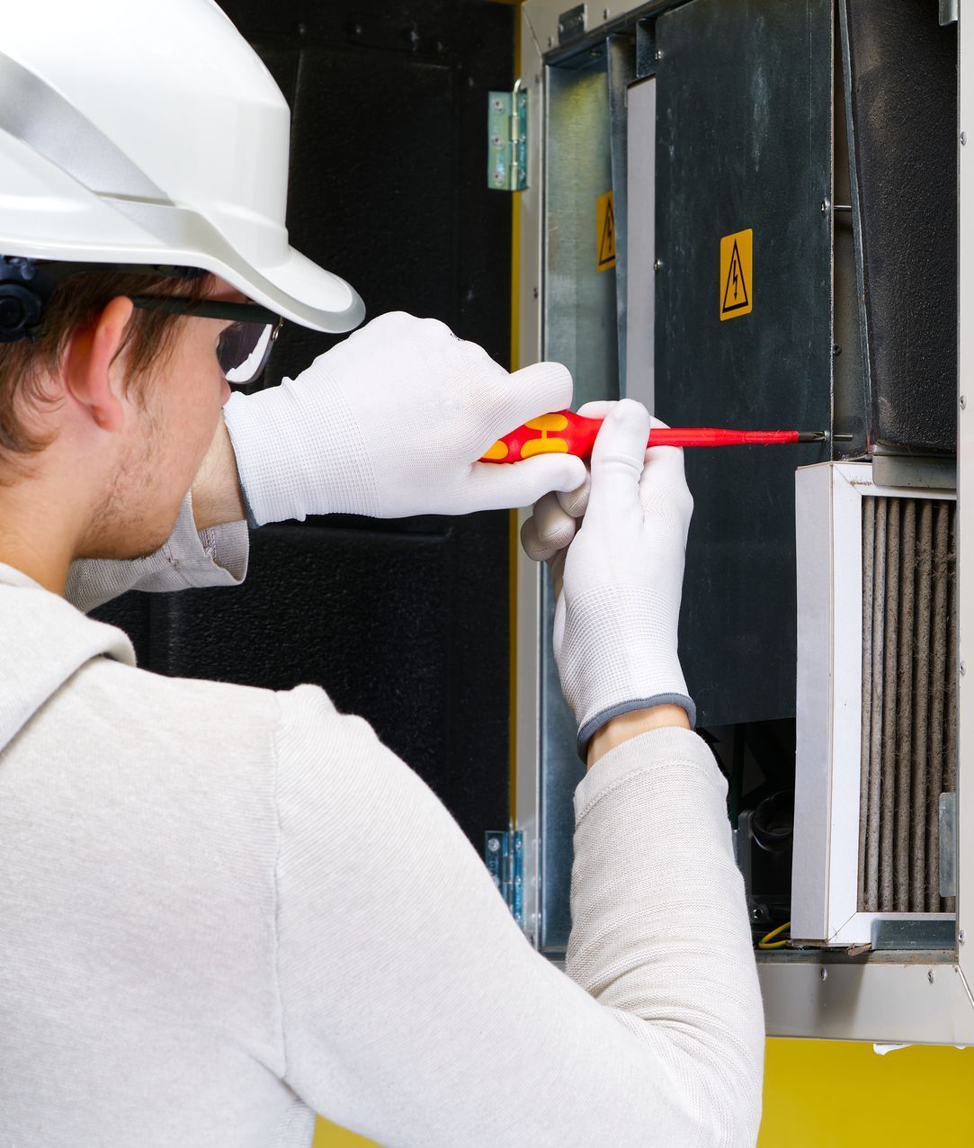 A man wearing a hard hat and gloves is holding a screwdriver